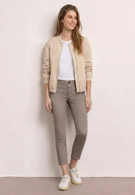 Jeune femme en look casual : blouson beige, t-shirt blanc, pantalon taupe et baskets blanches.