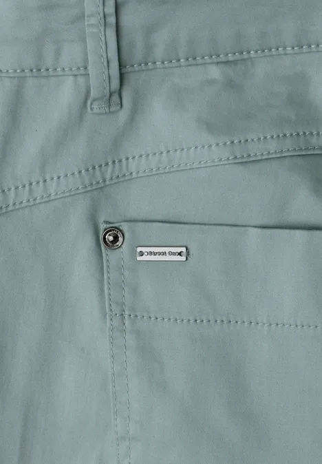 Close-up van een lichtgroene broek met zijzak en klein label.