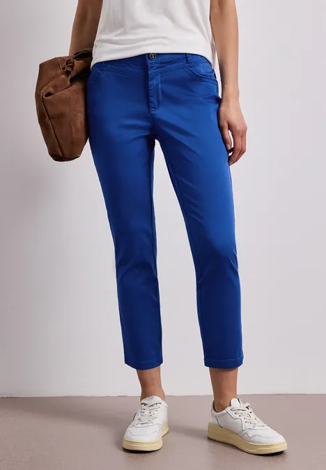 Vrouw draagt smalle blauwe 7/8-broek met witte sneakers.