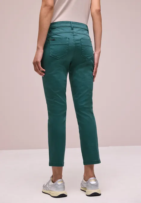 Person von hinten, trägt grüne Hose und weiße Sneaker vor schlichter Kulisse.