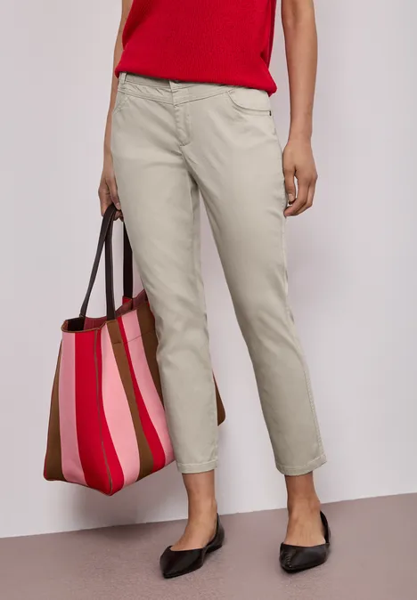 Vrouw in rood shirt, beige chino, zwarte ballerina's en gestreepte roze-rode shopper.