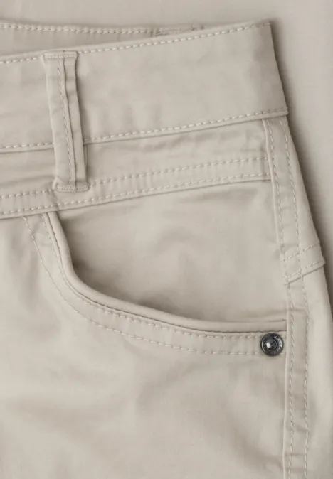Close-up van een beige broek met zichtbare zak, riemlussen en een metalen klinknagel