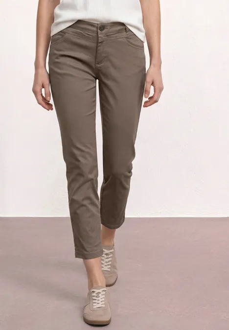 Vrouwelijk model draagt kaki chino en lichte sneakers voor witte achtergrond.