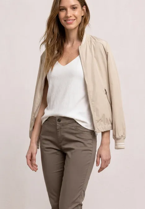 Een persoon in een casual look: wit topje, beige bomberjack en bruine chino.