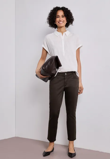 Vrouw draagt wit overhemd, zwarte broek, zwarte ballerina’s en houdt een zwarte clutch vast.