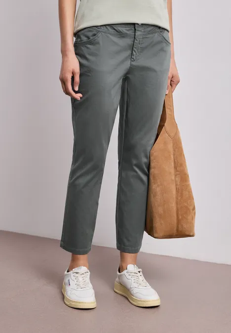 Persoon draagt grijze chino, witte sneakers en houdt een bruine suède tas vast.