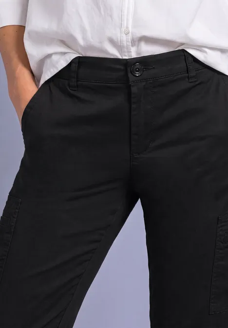 Spodnie typu chinos z wąskimi nogawkami i kieszeniami Cargo Black Model nosi czarne spodnie bojówki i białą koszulę, dłonie swobodnie w kieszeniach.