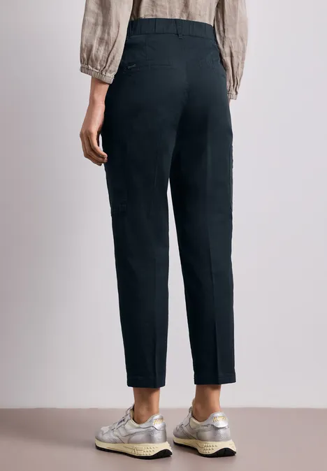 Een persoon van achteren draagt een zwarte, hoog getailleerde broek en lichte sneakers, minimalistische achtergrond.