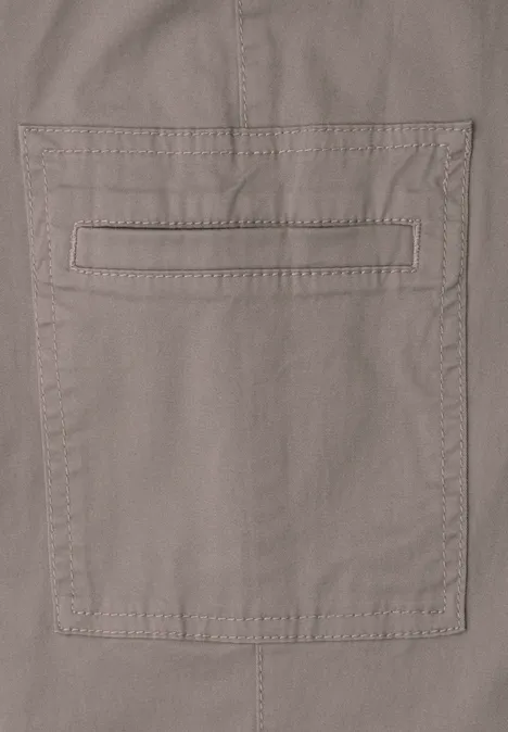 Close-up van een beige katoenen broek met opgestikte zak en subtiele sierstiksels.