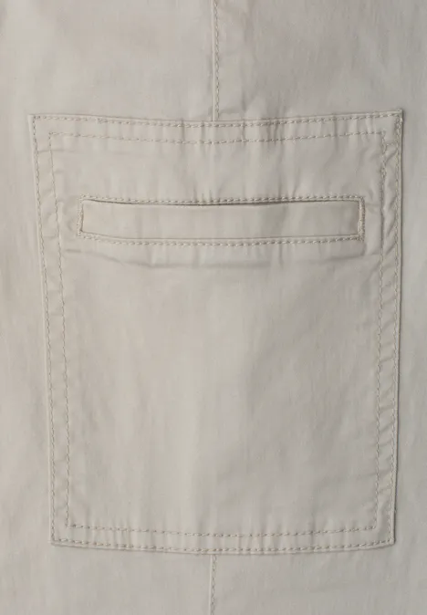 Beige katoenen stof met opgestikte zak en zichtbare sierstiksels.