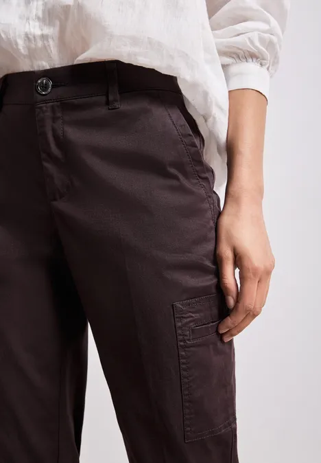 Close-up van een persoon met een bruine cargobroek en wit bovenstuk, hand langs de dij.