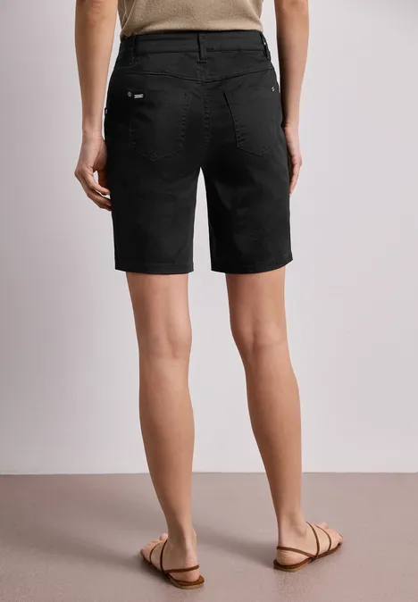 Achteraanzicht van een persoon in zwarte bermudashort en sandalen op een lichte vloer.