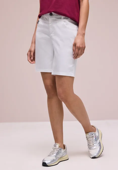 Vrouw draagt rood T-shirt, witte jeansshorts en zilveren sneakers.