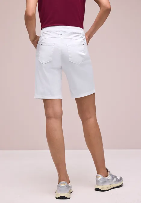 Een man van achteren in witte korte broek tot aan de knieën met grijze sneakers tegen een neutrale achtergrond.