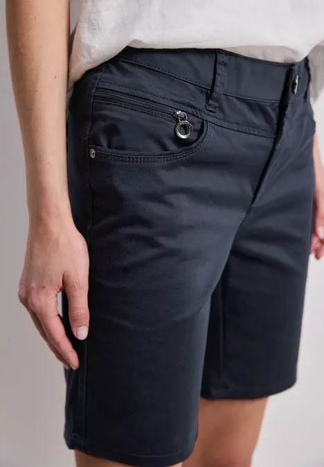 Een persoon draagt donkerblauwe bermudashorts met zakken en een lichtT-shirt.