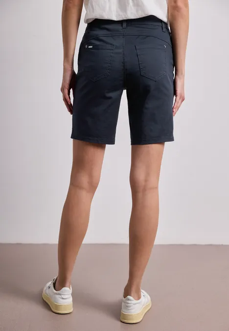 Iemand draagt donkerblauwe bermudashort, rugaanzicht met witte sneakers.