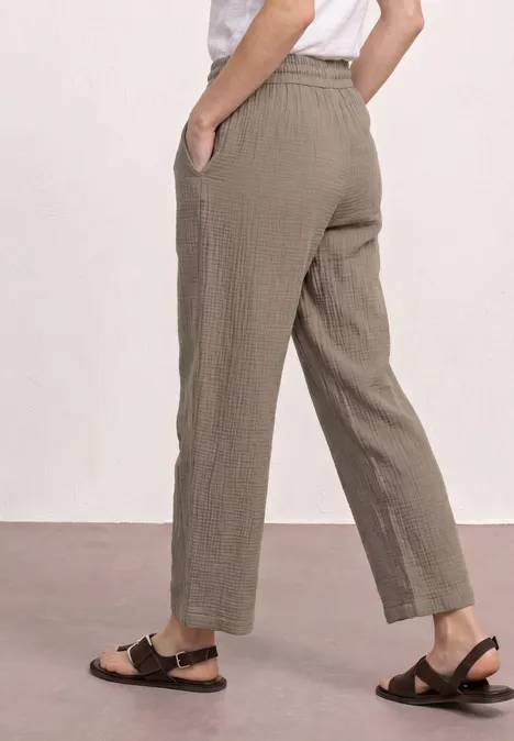 Seitenansicht: locker sitzende, knöchellange Hose in Olivbeige mit Taschen, dazu schwarze Riemchensandalen.