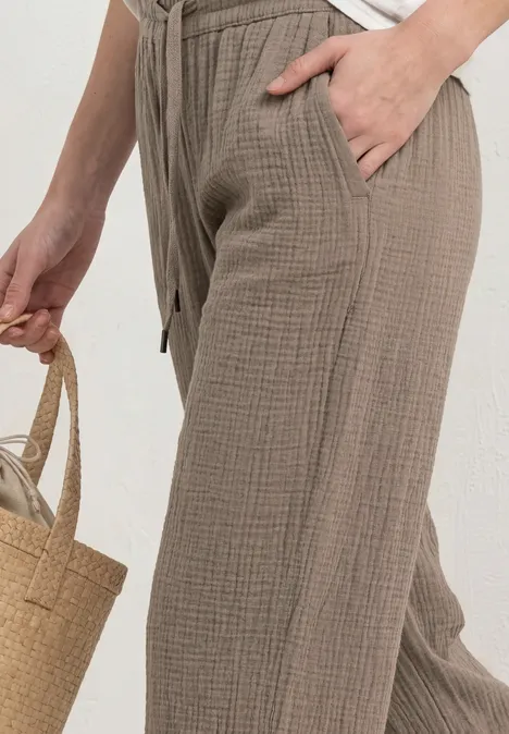 Frau trägt weite, beige Baumwollhose mit Tunnelzug und Taschen, hält einen Strohkorb