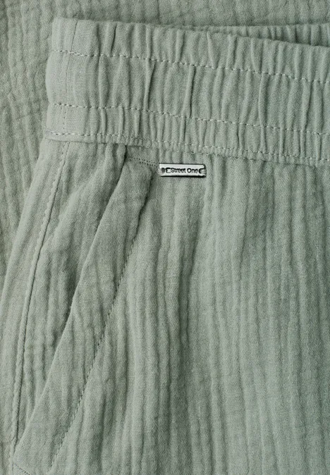 Detailaufnahme einer hellgrünen, strukturierten Hose mit elastischem Bund, Seitentasche und kleinem Markenlabel.