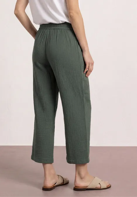 Frau von hinten in weiten, knöchellangen, gerippten, olivgrünen Hose und Sandalen.