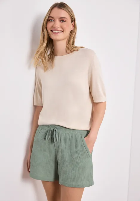 Eine Frau trägt einen hellen Kurzarm-Pullover und lockere grüne Shorts.