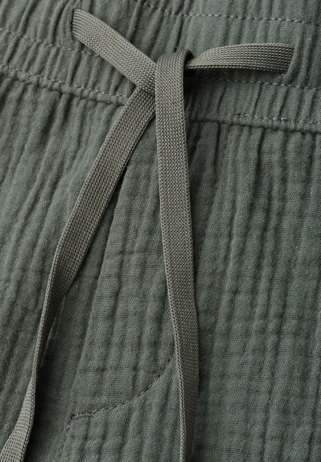 Nahaufnahme einer graugrünen, strukturierten Hose mit Kordelzug und seitlicher Tasche.