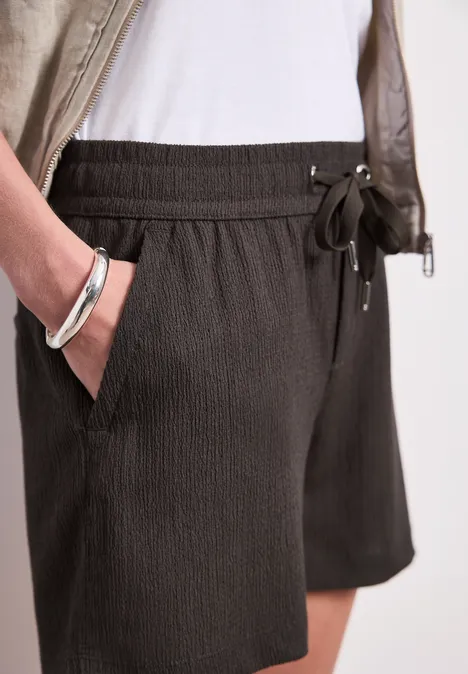 Dunkelgraue, strukturierte Shorts mit Tunnelzug und Seitentaschen, kombiniert mit weißem Top und silbernem Armreif.