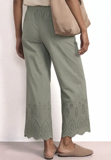 Rückenansicht einer Frau in grünen, weiten Culottes mit Lochstickerei am Saum, dazu Tasche und bequeme Schuhe.