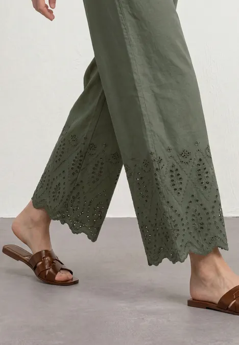 Frau trägt olivgrüne, bestickte Culotte mit gezacktem Saum und braune Sandalen.