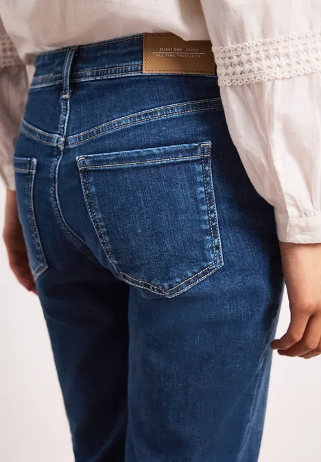Person von hinten in blauen Jeans und weißem Oberteil mit Spitzendetails.