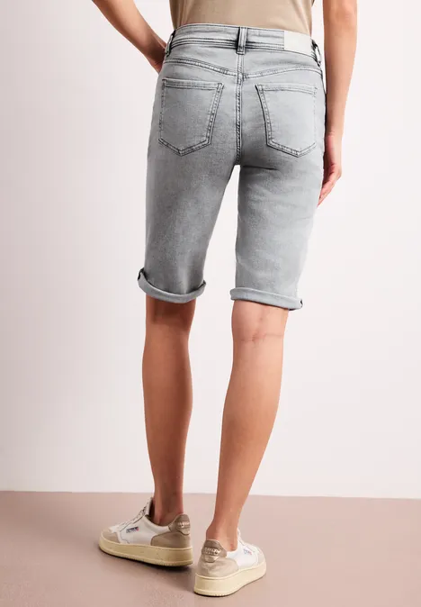 Rückansicht einer Person in grauen Jeans-Shorts mit umgeschlagenem Saum und beigen Sneakern.