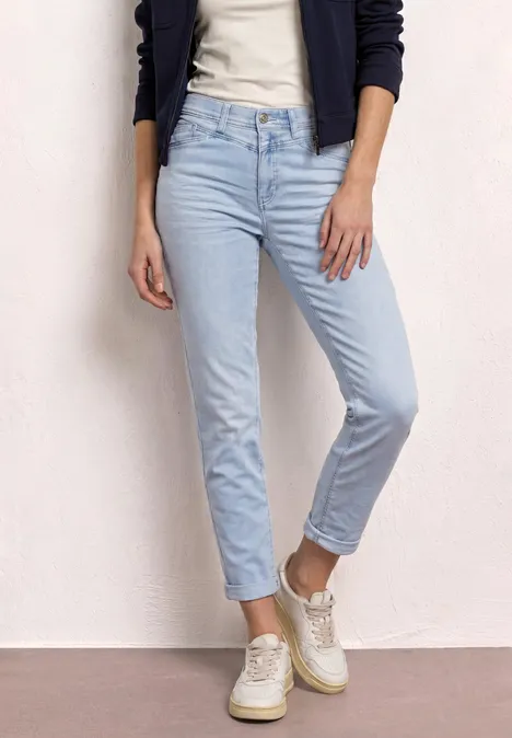 Person trägt hellblaue Jeans, weiße Sneaker, T-Shirt und dunkelblaue Strickjacke.