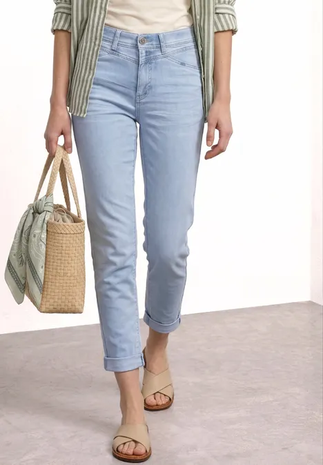 Frau in hellblauen Jeans und Sandalen hält eine Basttasche mit Tuch.