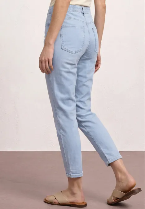 Frau von hinten in hellblauen Jeans und sandfarbenen Sandalen.