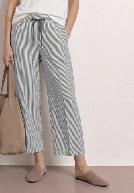 Femme portant un pantalon gris à rayures larges, top blanc, mules beiges et sac taupe.