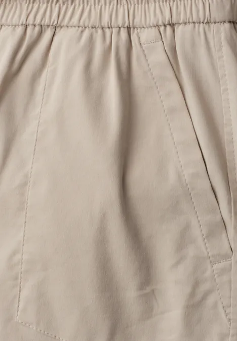 Detailansicht einer beigen Stoffhose mit elastischem Bund und seitlicher Eingrifftasche