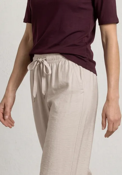 Personne portant un pantalon en lin beige à cordon et un t-shirt bordeaux sur fond clair uni.