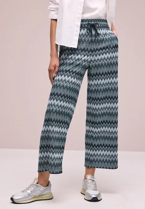 Weite Hose mit grün-blauem Zickzackmuster und weißen Sneakers.