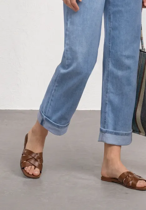 Füße in braunen, geflochtenen Ledersandalen und hochgekrempelten, hellblauen Jeans.