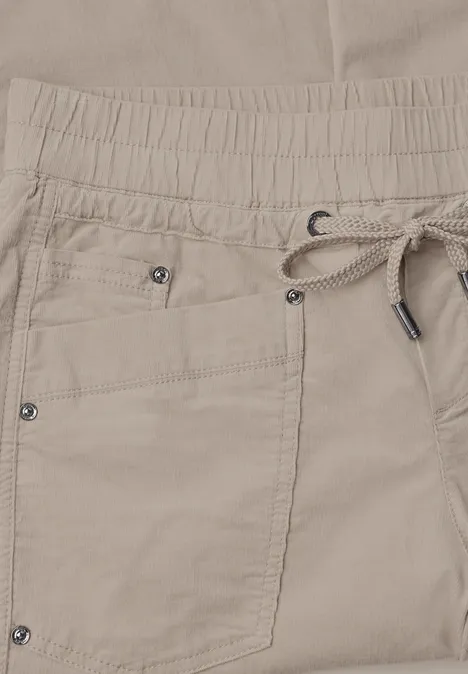 Beige Hose mit elastischem Bund, Kordelzug und aufgesetzter Tasche mit Metallnieten.