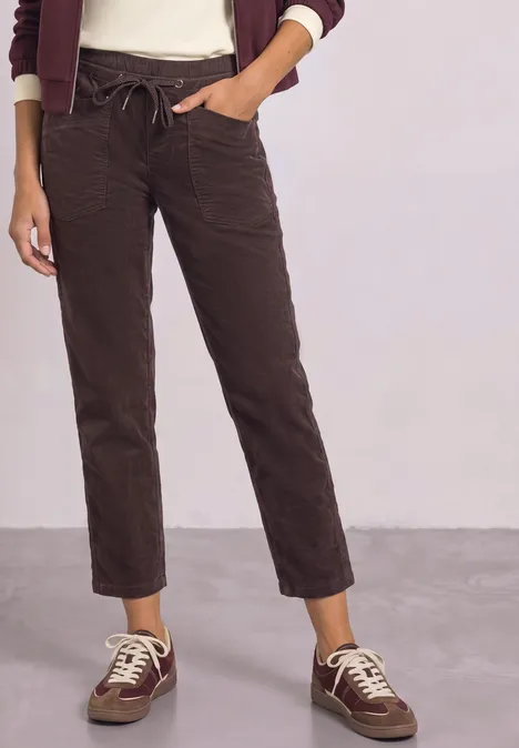 Eine Person trägt braune Cordhose mit Kordelzug und weiße Sneakers mit dunklen Details.