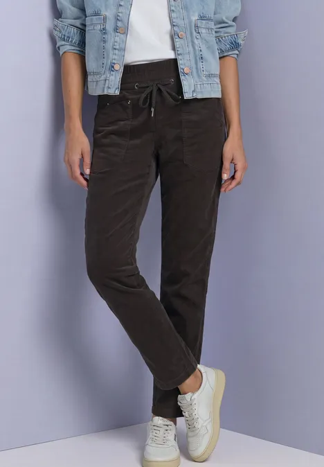 Slim Leg Cordhose im Loose Fit black coffee Person in dunkelbrauner Hose, weißem T-Shirt, Jeansjacke und weißen Sneakern vor hellem Hintergrund.