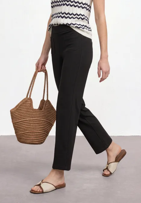 High Waist Straight Leg Hose im Casual Fit Black Frau in gemustertem Top, schwarzer Hose, flachen Sandalen und korbförmiger Handtasche