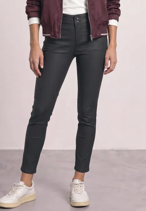 Jeans noires moulantes enduites, taille haute, ourlets aux chevilles et baskets blanches.