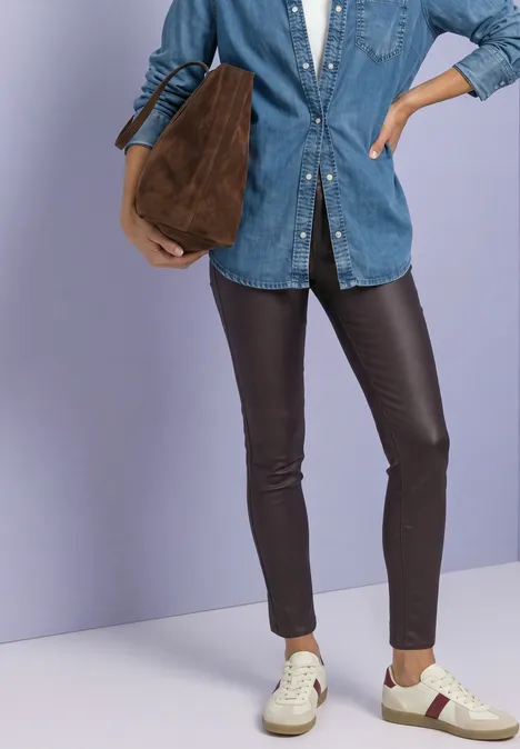 Eine Person mit Jeanshemd, schwarzen Lederleggings, weißen Sneakern und einer braunen Tasche.