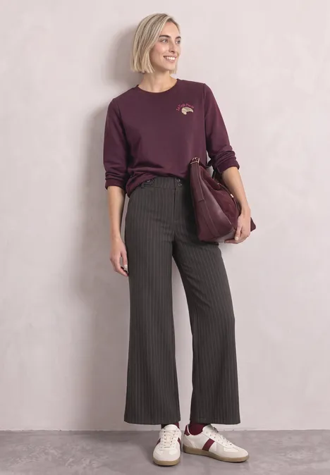 Femme en look décontracté chic : t-shirt bordeaux, pantalon large rayé noir, baskets blanches, sac bordeaux.