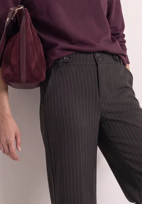 Personne porte pantalon à fines rayures gris foncé, haut violet et sac assorti.