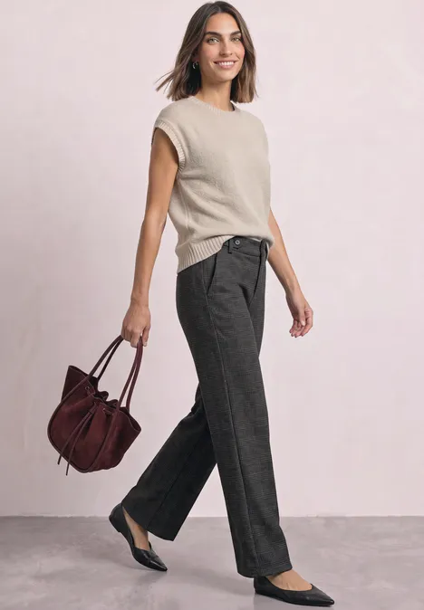 Femme en top beige et pantalon gris porte un sac bordeaux et des ballerines noires en marchant.