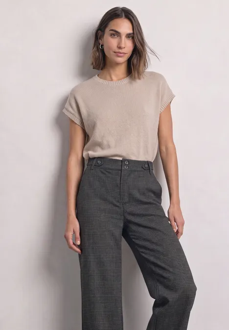 Femme en t-shirt beige et pantalon ample taille haute gris foncé devant un fond clair.