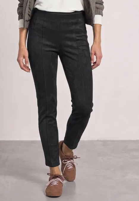 Personne porte un pantalon noir ajusté et des chaussures marron lacées, debout sur un sol gris.
